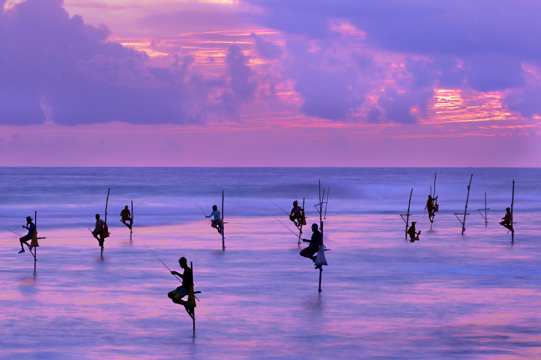 Fishermen on stilts in silhouette at the sunset in Galle